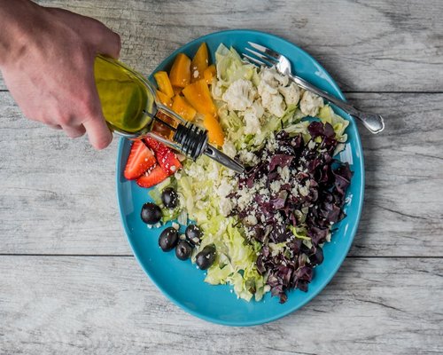 Person pouring olive oil on a fresh salad